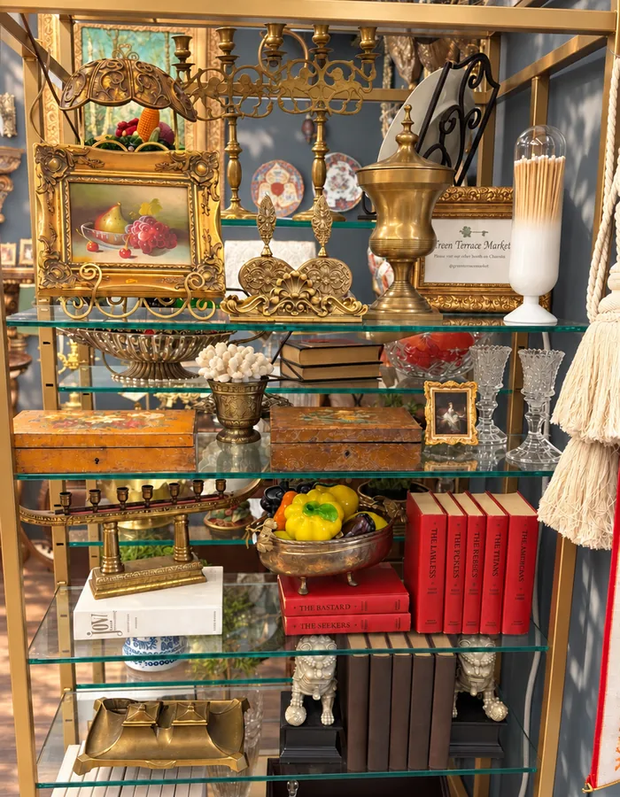 A gold etagere filled with brass candelabras, books and a fruit still life